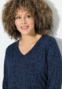 Top blu navy con scollatura a V, realizzato in un tessuto morbido con un motivo testurizzato di lettere di diverse dimensioni e orientamenti.