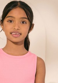 Ružové rebrované tielko bez rukávov s okrúhlym výstrihom, so hladkou textúrou a voľným strihom, nosené dieťaťom s hnedými vlasmi.