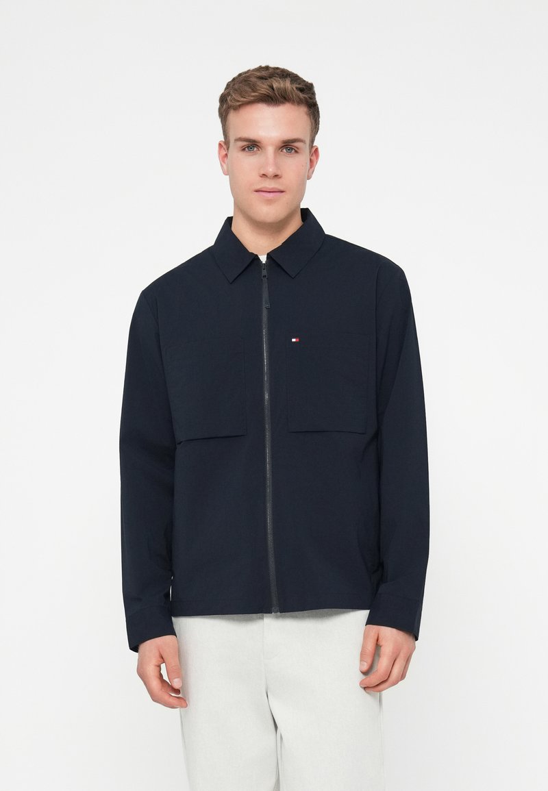 Ναυτική ζακέτα με φερμουάρ και γιακά, δύο μπροστινές τσέπες και μικρή διακοσμητική λογότυπο. Κατασκευασμένη από λεία, ελαφριά ύφασμα.