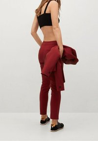 Pantalon ajusté bordeaux associé à un crop top noir et une veste assortie, avec des chaussures noires ornées d'un nœud. Tissu lisse, coupe sur mesure.