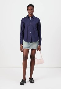 Camicia blu navy con maniche lunghe, abbinata a una mini gonna di denim. Accessoriata con una borsa rosa chiaro e mocassini neri.