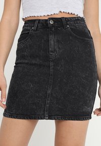 Falda de denim negro con un diseño ajustado, cierre frontal de botones y cinco bolsillos. Presenta una textura desgastada y un dobladillo recto.