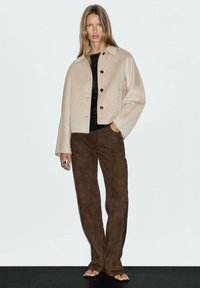 Beige wool-blend cropped jacket with black buttons, paired with brown suede wide-leg pants. Model stands against a light background.