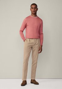 Helles rosa langärmliges Sweatshirt, beigefarbene Hose und braune Wildlederschuhe. Einfaches Design mit Rundhalsausschnitt und geradem Schnitt der Hose.