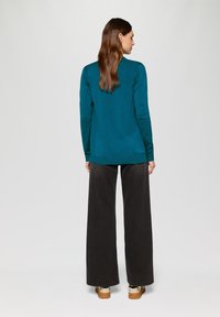 Türkiser Langarm-Top kombiniert mit schwarzen weit geschnittenen Hosen. Das Outfit zeichnet sich durch ein einfaches Design, einen weichen Stoff und eine lockere Passform aus.