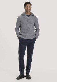 Grauer, gestrickter Pullover mit Kragen und halbem Reißverschluss, kombiniert mit marineblauen Cordhosen und schwarzen Stiefeletten. Glatte Textur und taillierte Passform.