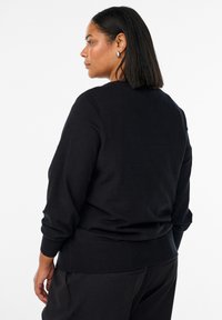 Čierny pletený sveter s okrúhlym výstrihom, voľnými rukávmi, rebrovaným lemom a stredne ťažkou látkou, v kombinácii s tmavými nohavicami.