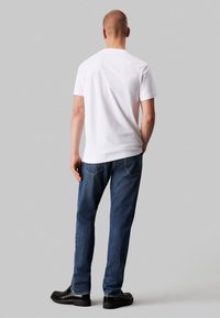 Camiseta blanca de cuello redondo combinada con jeans de mezclilla azules. Los jeans tienen un corte recto con una pierna ligeramente ajustada y costuras visibles.