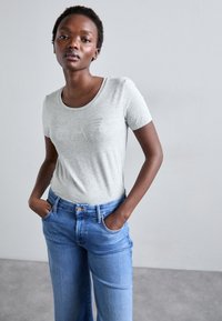 Tricou gri din bumbac cu mâneci scurte, cu un logo texturat "EA7" din strassuri, asociat cu blugi albaștri cu talie înaltă.