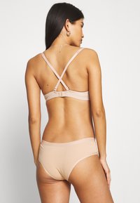 Beige underwear set featuring a cross-back bra with adjustable straps and a seamless hipster bottom, made from smooth, stretchy fabric.