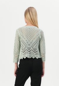 Lace-strickmintgrüner, kurz geschnittener Pullover mit gewelltem Saum und Dreiviertelärmlen, der mit filigranen Mustern und einem offenen Rücken gestaltet ist.