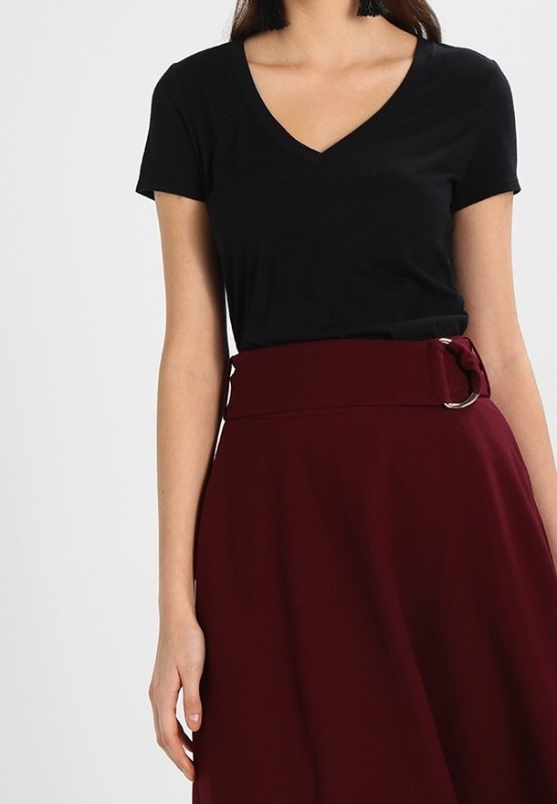 T-shirt noir à col en V associé à une jupe bordeaux taille haute avec une large ceinture et un détail de boucle métallique. Texture de tissu lisse.