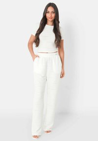 Witte, ribbelstof twee-delige set bestaande uit een crop top met korte mouwen en losse broek met zakken en een elastische tailleband.