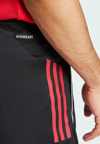 Schwarze Sportshorts mit rotem drei-streifigem Design, Aeroready-Logo und einer glatten Textur. Verstellbarer Bund und seitliche Tasche sichtbar.