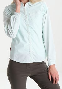 Camicia a maniche lunghe verde menta chiaro, con bottoni, caratterizzata da un delicato motivo a pois, una singola tasca sul petto e un orlo dritto.