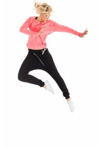 Pink sweatshirt with a loose fit and round neckline, paired with black jogger pants featuring an elastic waistband and ankle cuffs. White sneakers.
