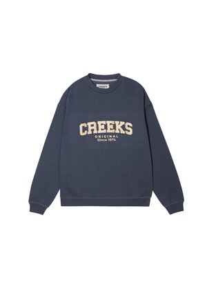Sudadera de marina con mangas largas, puños acanalados y cuello redondo. Presenta 'CREEKS ORIGINAL Desde 1974' en beige, impreso en la parte frontal.