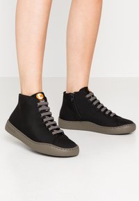 Czarne sneakersy typu high-top z szarymi sznurowadłami, materiałową cholewką, gumową podeszwą oraz zamkiem bocznym. Na języku znajduje się metka z logo.