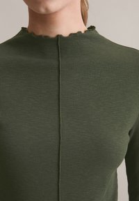 Groene geribbelde lange mouwen top met een geschulpte halslijn en een centrale naad. Gemaakt van een gestructureerde stof, die een getailleerde silhouet biedt.