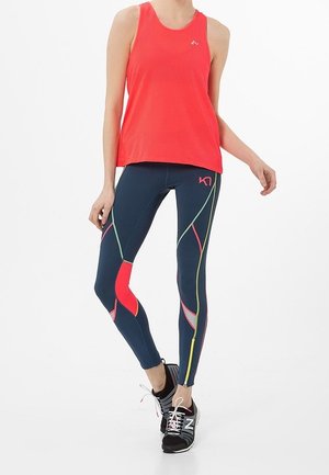 Canottiera rossa in rete, leggings blu navy con motivi geometrici colorati e scarpe da ginnastica nere. Focalizzazione su prestazioni e mobilità.