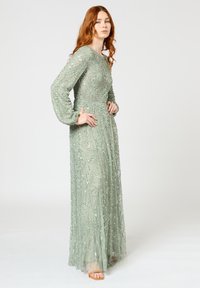 Lang, mintgroene jurk met ingewikkelde kraalwerk in bloemmotieven, met lange mouwen en een vloeiende silhouette.