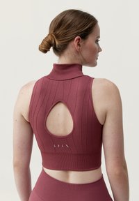 Bezramenný krCrop top v maroon odstínu s žebrovanou strukturou, s malým stojáčkem a výřezem na zádech. Obsahuje jemné logo v blízkosti spodního lemu.