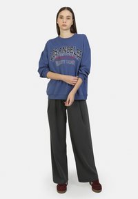 Sudadera azul con el gráfico "LOS ÁNGELES", combinada con pantalones de pierna ancha oscuros. Textura suave, corte casual y puños acanalados.