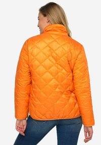 Giacca trapuntata di un brillante arancione con colletto alto, polsini a coste e forma aderente; presenta un motivo a rombi e una texture liscia.