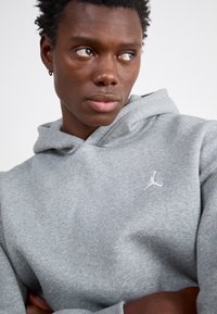 Hoodie gris en tissu mélange de coton, avec une poche avant et un logo Jumpman blanc sur la poitrine. Finition texturée avec une coupe décontractée.