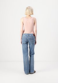 Pink ribbed tank top and light blue wide-leg jeans with back pockets, showcasing a relaxed fit and a slight fraying at the hem.