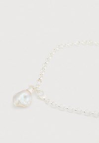 Ασημένιο βραχιόλι με αλυσίδα που φέρει ένα μενταγιόν μαργαριταριού με ακανόνιστο σχήμα και ιριδίζουσα όψη. Ο σχεδιασμός περιλαμβάνει κούμπωμα με κλιπ για ασφαλή κλείσιμο.