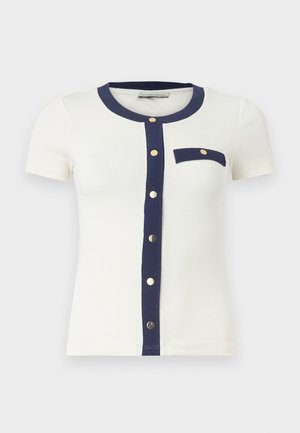 Λευκό τοπ με κοντά μανίκια και navy μπλε περιθώριο κατά μήκος του στρογγυλού λαιμού, κουμπωτή μπροστινή λωρίδα και μία θήκη στο στήθος με χρυσά κουμπιά.