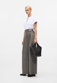 Weißes kurzärmeliges Oberteil mit einem Schlüssel-Ausschnitt, hochgeschnittene graue weite Hose und eine schwarze strukturierte Handtasche mit dekorativen Nieten.