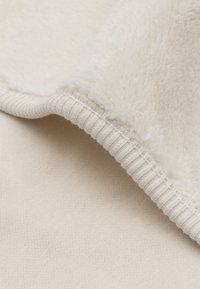 Fleece dekentje met een zachte, crèmekleurige textuur aan de bovenkant en een gladde, crèmekleurige onderkant. Heeft een ribbelrand voor een stevige afwerking.