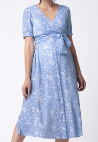 Světle modré šaty s krátkými rukávy, výstřihem do V, květinovým vzorem v bílé barvě, detailem na uvázání v pase a knoflíkovým zapínáním na sukni.
