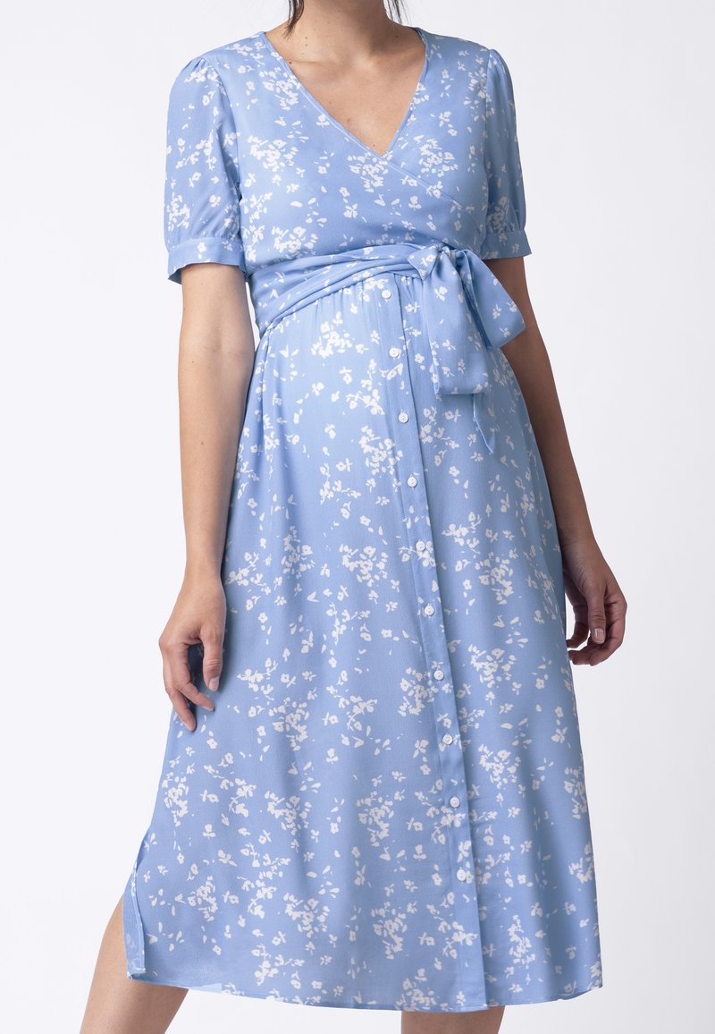 Světle modré šaty s krátkými rukávy, výstřihem do V, květinovým vzorem v bílé barvě, detailem na uvázání v pase a knoflíkovým zapínáním na sukni.