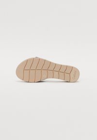 Shoe sole made of rubber, with a beige color and patterned grooves for traction. Features brand logo and embossed details along the edge.