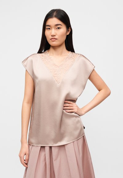 Τοπ από ανοιχτό καφέ σατέν με λαιμόκοψη σε σχήμα V, που διαθέτει λεπτεπίλεπτες δαντέλες. Κοντά μανίκια και άνετη γραμμή συμπληρώνουν το σχέδιο.
