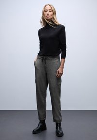 Czarny sweter z golfem w połączeniu z szarymi spodniami cargo ze zwężanymi nogawkami i kieszeniami. Modelka nosi czarne botki za kostkę. Prosty, casualowy zestaw.