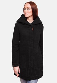 Black wool coat with a large hood, side pockets, and front closure. Notable texture and a small logo near the neckline.