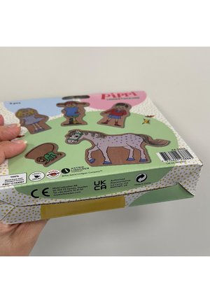 Hand hält eine bunte Schachtel mit hölzernen Pippi Langstrumpf-Figuren, einschließlich eines Pferds und vier ausgeschnittenen Figuren.