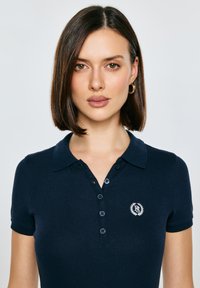 Námořnicky modré polo tričko s límečkem, krátkými rukávy, žebrovanou texturou a malým vyšívaným logem na hrudi.