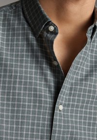 Camicia a quadri verde e bianca con colletto classico, dotata di bottoni simili a perle e una texture di tessuto morbido.