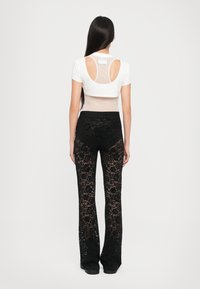 Λευκό κοντομάνικο μπλουζάκι με σχέδιο κομμένου πίσω μέρους και διάφανη ύφανση, συνδυασμένο με μαύρα κεντημένα φλοράλ παντελόνια με φούντες.