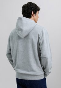 Sudadera con capucha gris de tejido texturizado, manga larga y puños y bajo de canalé; presenta una costura en la parte central de la espalda y una capucha profunda.