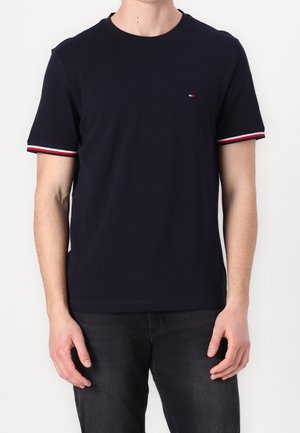 Námorně modré bavlněné tričko s krátkým rukávem, zdobené bílými a červenými pruhy na manžetách a malým logem na hrudi.