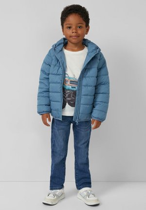 Gevoerde blauwe jas met een capuchon, met rits aan de voorkant, gedragen over een witte graphic t-shirt, gecombineerd met blauwe jeans en witte sneakers.