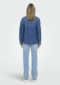 Donkerblauwe denimshirt met een knoopsluiting aan de voorkant, lange mouwen en een gebogen zoom. Gecombineerd met lichtblauwe recht gesneden jeans.