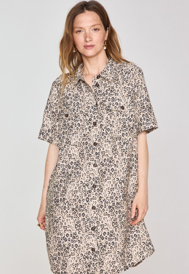 Abito camicia a maniche corte in beige chiaro con stampa leopardata nera, dotato di chiusura frontale con bottoni e due tasche sul petto. Tessuto morbido.