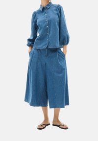 Conjunto de denim que presenta una camisa azul clara, con botones y mangas abullonadas, acompañada de culottes de pierna ancha. El material es suave y tiene detalles de costura visibles.
